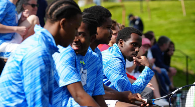 A group of young men sitting on a bench with tennis rackets.