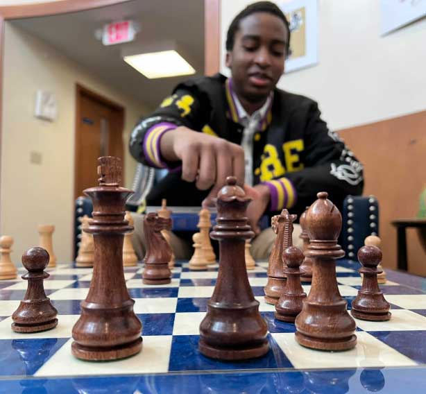 A young man playing chess on a blue board.