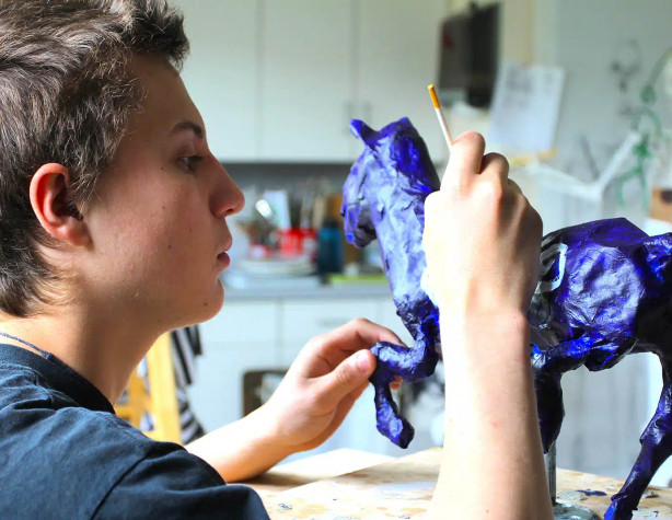 A boy is painting a blue horse.