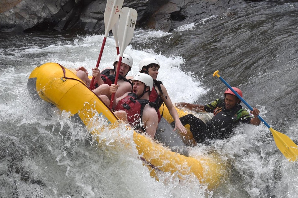 Four people wearing helmets and life jackets are white-water rafting in a yellow inflatable boat, navigating rough rapids—an adventure that, like individualized learning, requires teamwork and adapting to challenges.