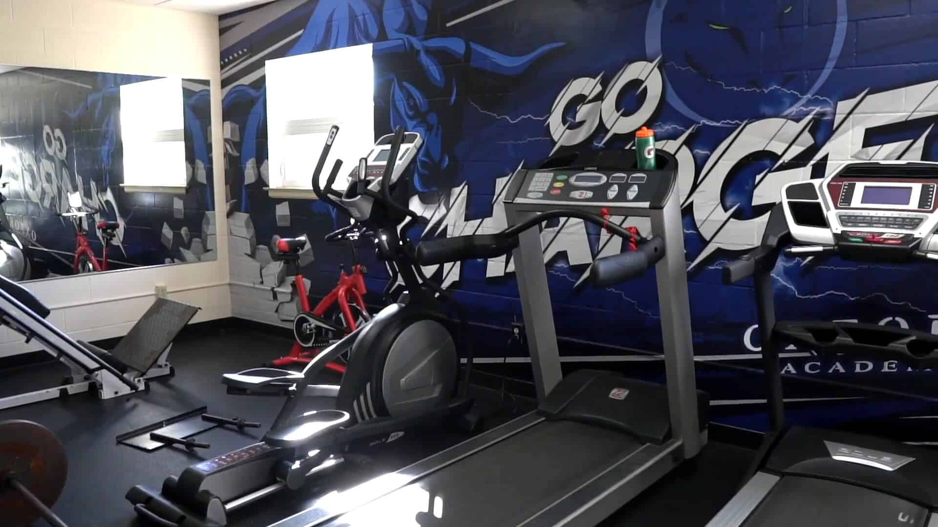 Fitness room with treadmills, an elliptical machine, a stationary bike, and a wall mural that says "GO WARRIOR"—perfect for elevating your Summer Experience.
