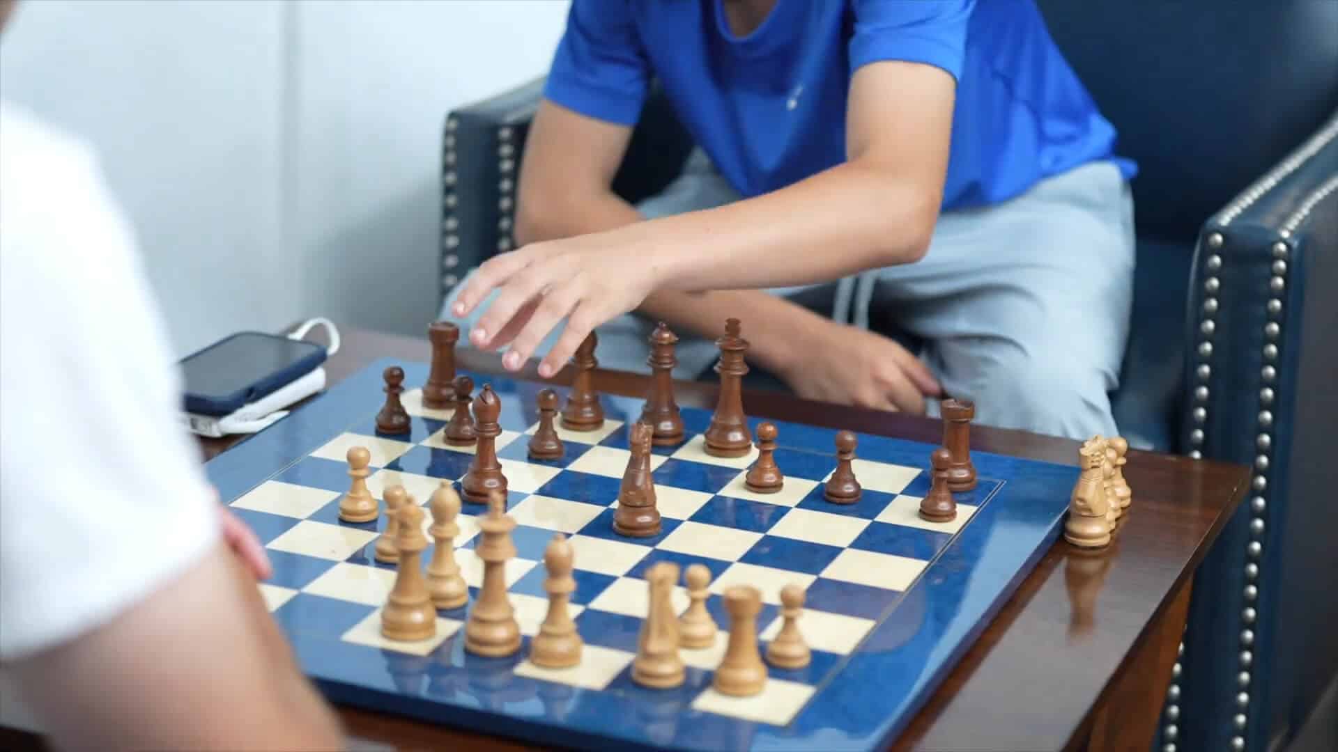 Two people enjoy a summer experience playing chess at a small table; one in a blue shirt makes a move while the other watches.